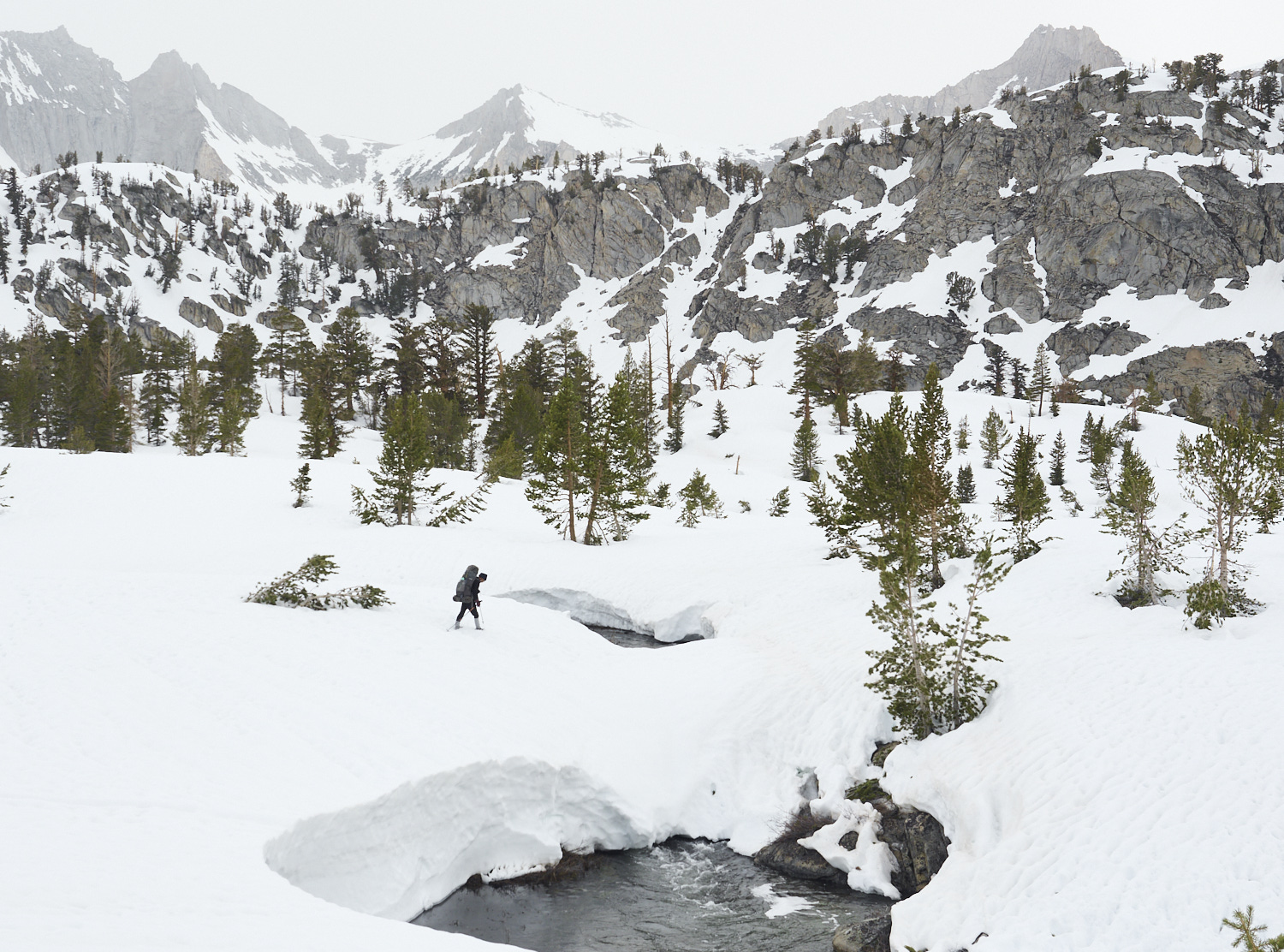 Ein Wanderer überquert in der tiefverschneiten Sierra Nevada einen Fluss über eine Schneebrücke