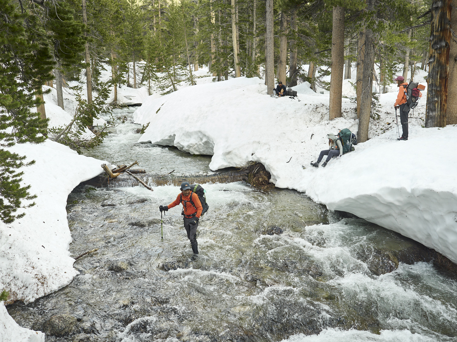 Ein Wanderer durchquert einen Fluss in der verschneiten Landschaft.