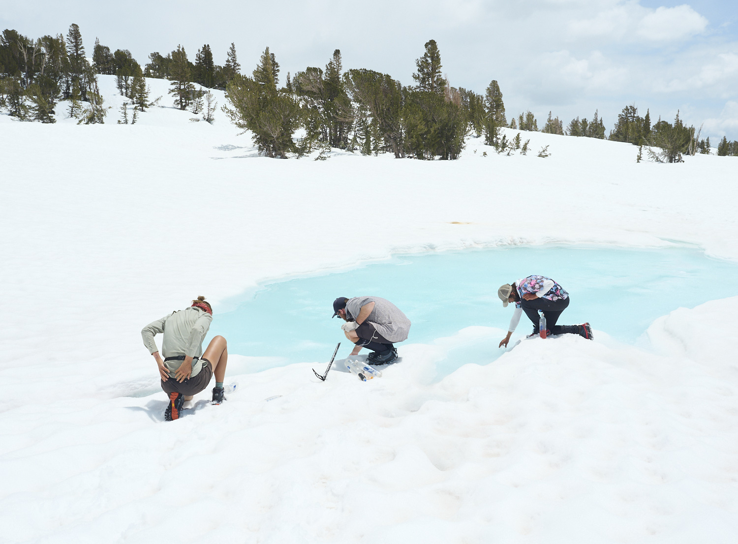 Wanderer nutzen eine aufgetaute Stelle eines gefrorenen und schneebedeckten Sees um Wasser aufzufüllen