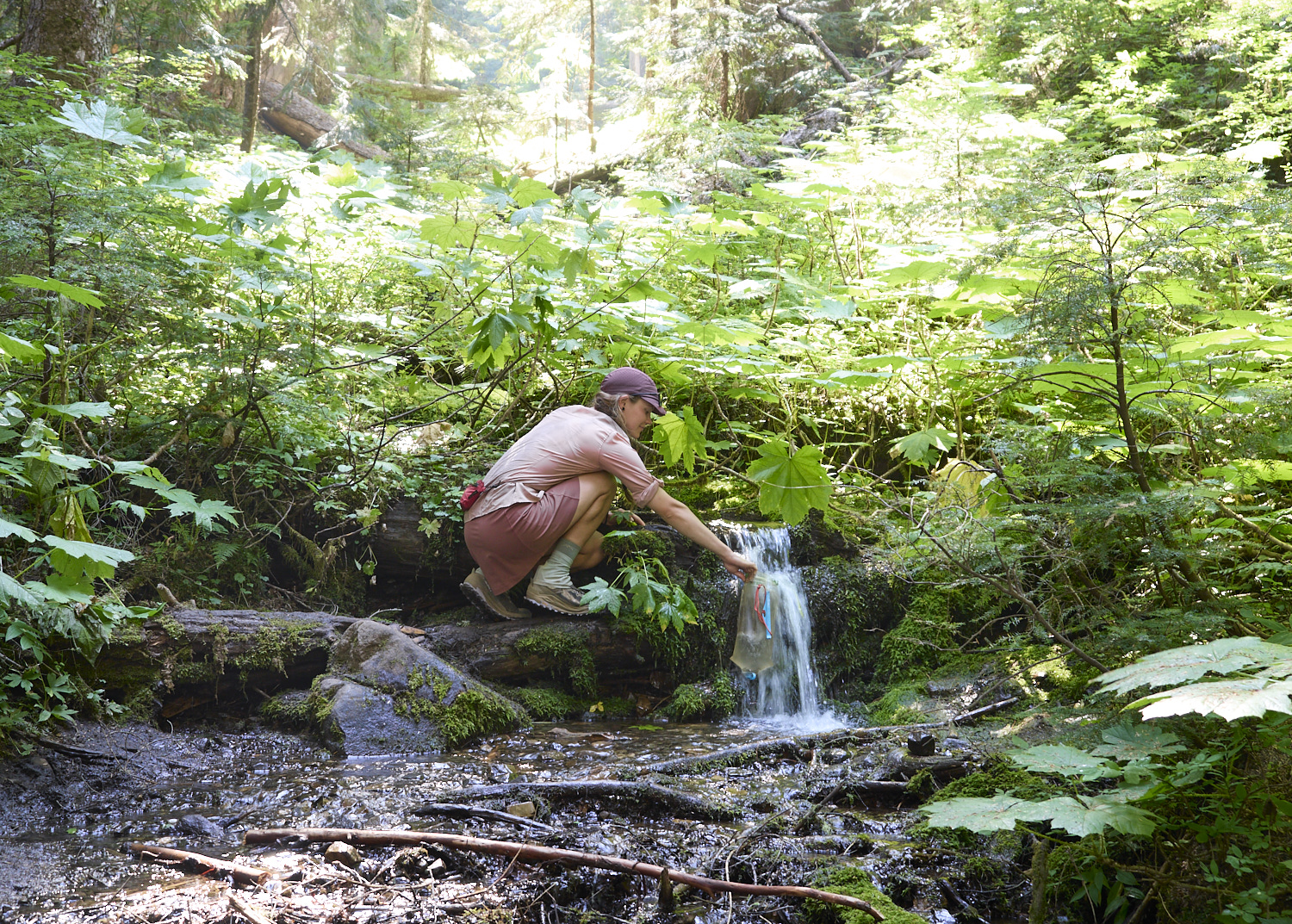 eine Wanderin füllt Wasser in einem Bach auf